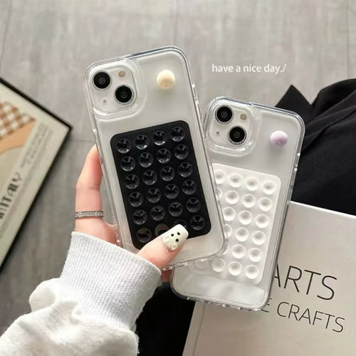 Two clear phone cases with 3D bubble designs are held in a hand. One case has a black bubble pattern and a small cream-colored bubble accent, while the other has a white bubble pattern and a small lavender bubble accent.